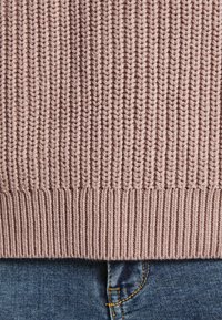 Pull en maille rose doux avec un motif texturé et une bordure côtelée, associé à un jean denim bleu avec des détails de couture subtils.