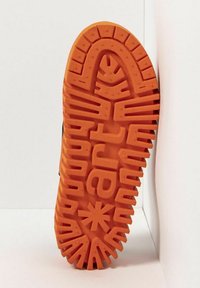 La semelle en caoutchouc présente une couleur orange avec des rainures profondes et des motifs de bande de roulement uniques, y compris des formes alphanumériques et un accent en forme d'étoile.