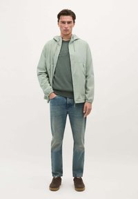 Lys grøn zip-up jakke med hætte, parret med en mørkegrøn sweatshirts, blå jeans og brune sko. Casual, afslappet pasform.