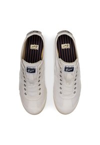 White canvas sneakers with round metal eyelets, beige rubber soles, and a tongue label featuring "Onitsuka Tiger" in black.