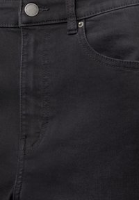 Gros plan sur le devant d’un jean en denim noir avec bouton métallique, passant de ceinture et détail de poche cousu.