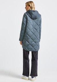 Vadderad petrolblå jacka med huva, med en något utsvängd nederkant och framträdande diagonala sömmar. Matcher med mörka jeans.