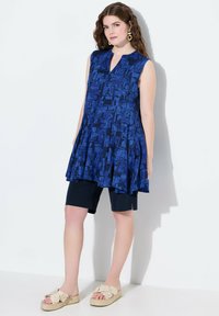 Tunica senza maniche blu navy con motivo geometrico, abbinata a pantaloni corti neri e sandali espadrillas floreali beige. Tessuto morbido, vestibilità comoda.