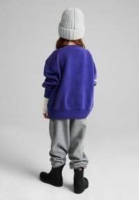 Fioletowa oversizeowa bluza, szare spodnie dresowe i czarne buty. Wełniana prążkowana czapka w jasnoniebieskim kolorze. Miękkie faktury, swobodny krój.