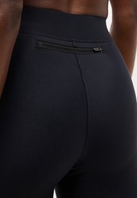 Κοντινό πλάνο ενός ατόμου που φοράει μαύρο αθλητικό κολάν με μια μικρή οριζόντια τσέπη με φερμουάρ στη ζώνη της μέσης στο πάνω μέρος της πλάτης.