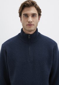 Navy fleece quarter-zip pullover with a high collar and textured finish. Features a black zipper at the neck and ribbed accents.