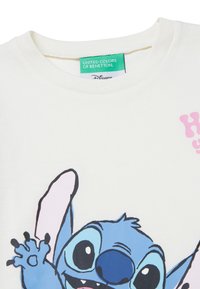 T-shirt bianca in cotone con scollatura rotonda, caratterizzata da un'illustrazione colorata di Stitch della Disney, con toni blu e accenti rosa.