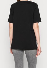 Svart kortärmad T-shirt, tillverkad av bomull, har en avslappnad passform och rund halsringning. Baksidan visar rena linjer utan grafik eller dekorationer.