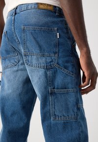 Blå denim cargo bukser med flere lommer, en normal pasform, synlige sømme og et mærke på taljen.