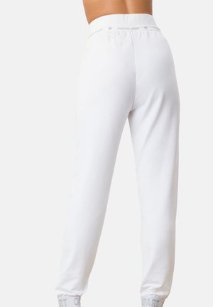Kvinde iført hvide højttaljede joggingbukser med elastisk talje og manchetter, vist bagfra mod en ensfarvet baggrund.