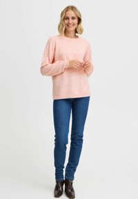 Maglione rosa chiaro, tessuto testurizzato, con maniche lunghe, collo tondo e orlo a coste, abbinato a jeans skinny in denim blu e stivali neri alla caviglia.