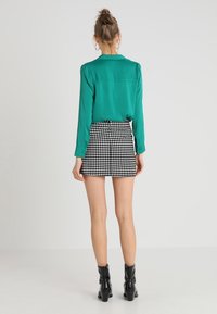 Blusa teal con maniche lunghe, dettaglio alla schiena, abbinata a una mini gonna in tessuto houndstooth bianco e nero. Stivali neri alla caviglia completano il look.