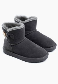 Botines de ante negros con forro de piel de oveja gris suave, con detalles de costura y un toggle de madera decorativo en el costado, que cuentan con una suela plana de goma.