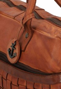 Bolso de cuero marrón tipo duffel con textura trenzada, cierre de cremallera y un emblema de ancla en una etiqueta circular de cuero. Asas sujetas de forma segura.