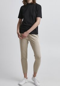 T-shirt noir à manches courtes en coton, associé à un pantalon de jogging slim beige. Chaussures de sport blanches. Design minimaliste sans motifs.