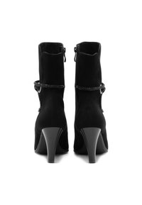 Schwarze Wildleder-Ankle Boots mit spitzer Zehe, hohen Absatz, samtiger Textur und dekorativem Riemen mit Akzenten. Reißverschluss auf der Innenseite.