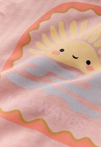 Leende sol med slutna ögon och rosiga kinder ovanför ett blått moln på rosa tyg med orange och gul vågig kant.
