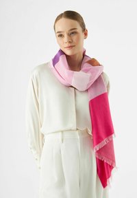 Écharpe colorée présentant des nuances de rose, de violet et de marron ; texture douce avec des bords frangés, drapée de manière décontractée autour du cou.