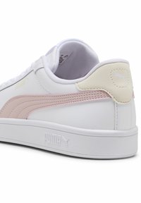 Sneaker bianco con una striscia rosa pallido e un accento panna sul tallone. Presenta una suola bianca texturizzata e un logo in rilievo sul lato.