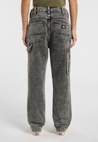 Jeans grises de pierna ancha con un acabado desgastado, costuras visibles, dos bolsillos traseros, un bolsillo lateral y una pequeña etiqueta de la marca cerca de la cintura.