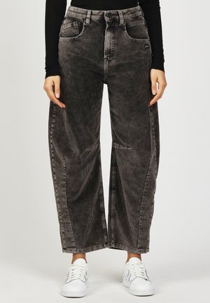 Person wearing black long-sleeve top, loose dark gray corduroy pants, and white sneakers, standing with hands relaxed by sides.