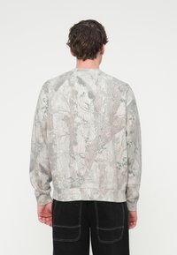 Γκρι φούτερ με καμουφλάζ μ οτίβο σε αποχρώσεις γκρι και μπεζ. Κατασκευασμένο από βαμβάκι, με άνετη εφαρμογή και μανσέτες με ριμπ ύφανση.