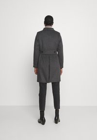 Szary wełniany płaszcz z paskiem w talii, guzikami na plecach i kołnierzem. Połączony z ciemnymi dżinsami i botkami za kostkę.