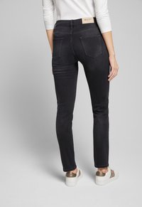 Schwarze Denim-Jeans mit schmalem Schnitt, mittelhoher Taille und Gesäßtaschen. Kombiniert mit weißen Sneakers mit einem goldenen Akzent an der Ferse.