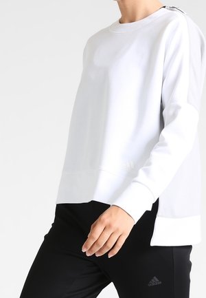 Sweatshirt blanc à coupe décontractée, avec des poignets côtelés et un logo en bas à gauche. Il présente une texture lisse et un détail de zip distinct sur le côté.