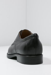 Chaussure en cuir noir à finition lisse, talon arrondi et détails de couture subtils ; présente un design minimaliste et une semelle robuste.