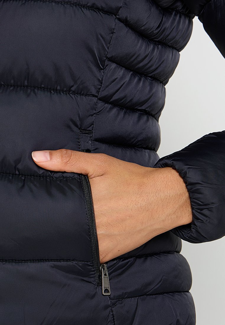 Giacca nera imbottita con design trapuntato, dotata di una tasca laterale con zip e polsini elasticizzati. Materiale liscio e leggero con una leggera lucentezza.