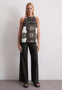 Top sin mangas en blanco y negro con patrones circulares, escote fruncido, combinado con pantalones anchos negros y sandalias negras texturizadas.