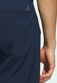 Marineblauwe shorts met een gestructureerde stof, zijzak en een Adidas-logo accent aan de achterkant. Hand geplaatst nabij de tailleband.