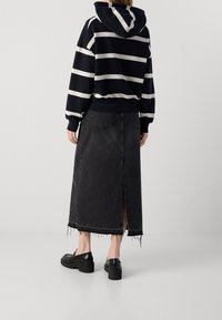 Falda de mezclilla negra con dobladillo desflecado y abertura trasera, combinada con una sudadera con capucha azul marino a rayas, con cordón en la capucha y puños acanalados. Zapatos de plataforma negros.