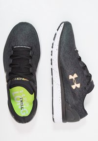 Chaussures de course noires avec une tige texturée, dotées d'une semelle intermédiaire blanche mouchetée et d'un logo doré. Semelle intérieure verte avec l'inscription « RUN LONG ».