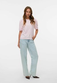 Ljusrosa topp med pösiga korta ärmar, som har ett diamantformat mönster, i kombination med ljusblå vida jeans och bruna spetsiga skor.