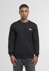 Zwarte sweatshirt met een ronde halslijn, ribgebreide manchetten en zoom, en een klein logopatch op de borst. Textuurstof, casual pasvorm.
