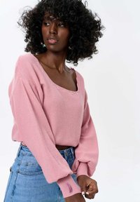 Roze gebreide trui met een boxy pasvorm, wijde halslijn en pofmouwen. Gecombineerd met hoge spijkerbroeken voor een casual look.