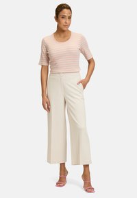 Light pink striped short-sleeve top paired with white wide-leg trousers. Includes side pockets and pink strappy sandals. Smooth texture overall.