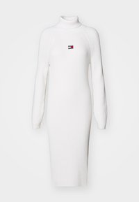 Vestido de punto blanco con cuello alto y mangas largas, que presenta un pequeño logo bordado en el pecho. Diseño ajustado.