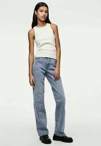 Weißes ärmelloses Oberteil, hellblaue gerade Jeans und schwarze klobige Stiefel. Glattes Material und lässige Passform mit minimaler Ausstattung.