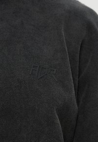 Crni teksturirani pulover s povišenim crnim "ADR" logom na prsima. Jednostavan dizajn bez dodatnih uzoraka ili akcenta.