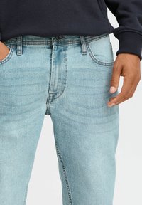 Vaqueros de denim azul claro con corte recto, bolsillos delanteros y cierre de botón estándar con detalles de costura en contraste.
