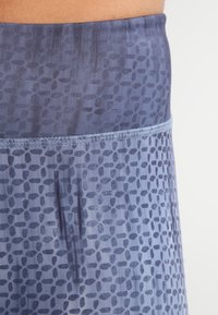 Niebieska tkanina w wzory z teksturowanym pasem i geometrycznym nadrukiem. Posiada szczegół kieszeni z boku, zaprojektowany z myślą o komforcie.