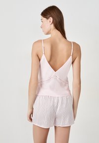 Jasnoróżowa satynowa koszulka na ramiączkach z koronkowymi zdobieniami w talii, zestawiona z białymi szortami z cienkimi pionowymi paskami w kolorze niebieskim i czerwonym.