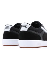 Svarte Vans joggesko med semsket skinn og nettdesign, hvite detaljer og gummisåler med brunt grep. Logo vist på hælen.