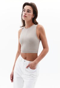 Top corto a coste beige con scollo rotondo e design senza maniche, abbinato a pantaloni bianchi a vita alta. Tessuto texturizzato e silhouette aderente.