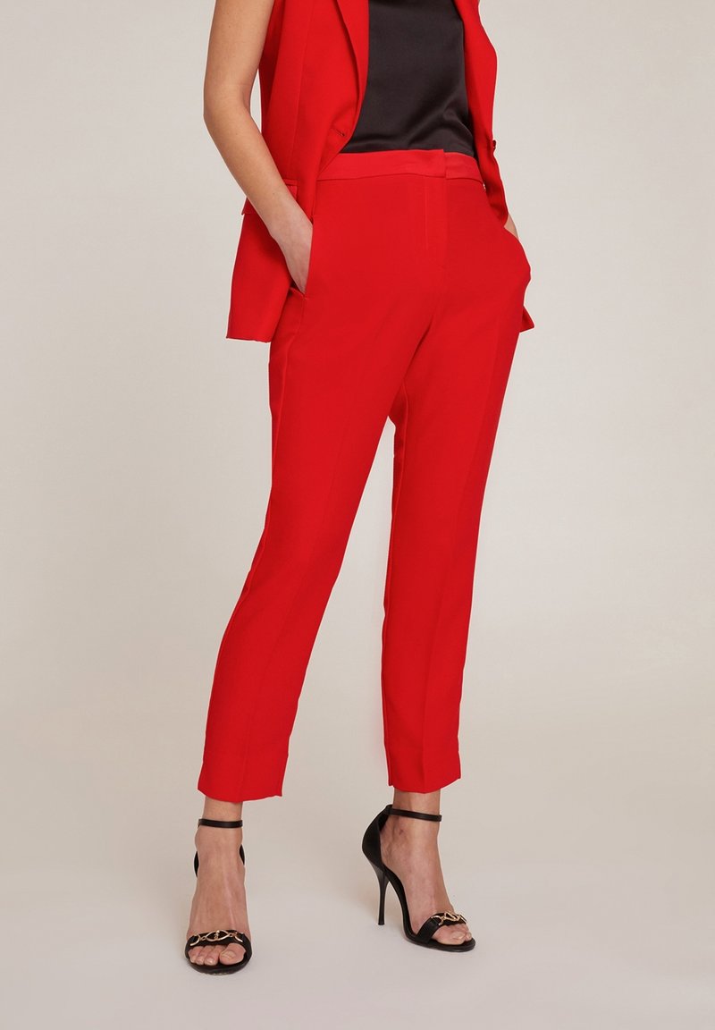 Röda skräddarsydda byxor i slät tyg med smal passform, med sidofickor och ankellånga avslut, i kombination med svarta högklackade sandaler.