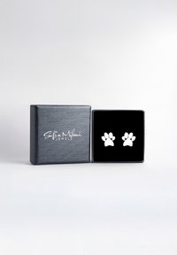 Orecchini a forma di zampa d'argento esposti in una scatola foderata di velluto nero, con un esterno nero testurizzato che presenta un logo bianco.