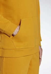 Hoodie jaune en coton avec poignets et ourlet côtelés. Comprend une poche avant et une texture lisse, mettant en valeur la simplicité du design.